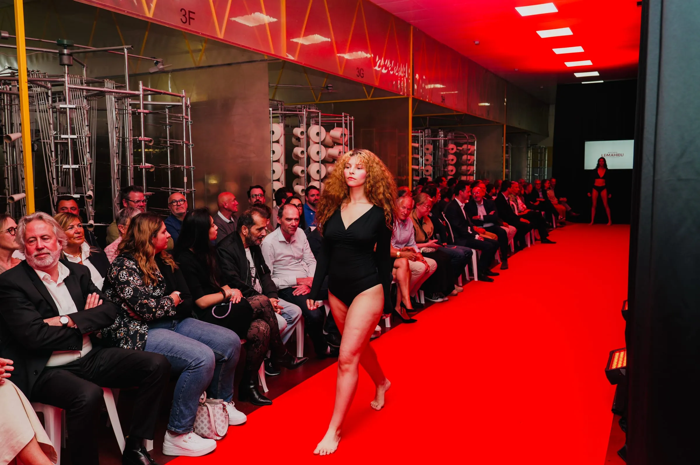 Mannequin en body noir défilant sur le tapis rouge entre les métiers à tricoter